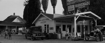 Movie still from “Nixon” (1995), directed by Oliver Stone – An old photo of a man walking in front of a service station; Extreme Wide shot, Low angle
