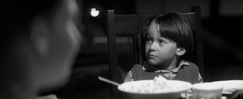 Movie still from “Nixon” (1995), directed by Oliver Stone – A little boy sitting at a table with a bowl of cereal; Close Up shot, Over the shoulder angle