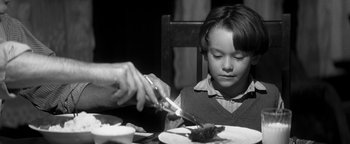 Movie still from “Nixon” (1995), directed by Oliver Stone – A person cutting a piece of food with a knife and fork; Close Up shot, Over the shoulder angle