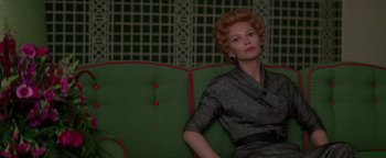 Movie still from “Nixon” (1995), directed by Oliver Stone – A woman sitting on a green couch in a room; Medium shot, Low angle