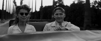 Movie still from “Nixon” (1995), directed by Oliver Stone – A young man sitting in a car wearing a suit and tie; Close Up shot, Low angle