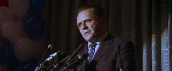 Movie still from “Nixon” (1995), directed by Oliver Stone – A man in a suit and tie speaking into microphones in front of microphones; Close Up shot, Low angle