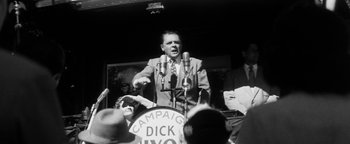 Movie still from “Nixon” (1995), directed by Oliver Stone – An old photo of a man speaking at a political event; Medium shot, Low angle