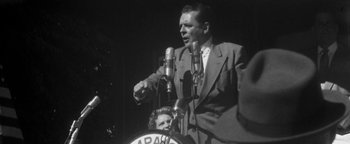Movie still from “Nixon” (1995), directed by Oliver Stone – An old photo of a man and a woman at a microphone; Medium shot, Low angle