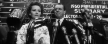 Movie still from “Nixon” (1995), directed by Oliver Stone – A man and a woman standing in front of microphones; Close Up shot, Over the shoulder angle