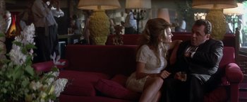 Movie still from “Nixon” (1995), directed by Oliver Stone – A woman sitting on top of a red couch next to another woman; Medium shot, Over the shoulder angle