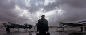 Movie still from “Nixon” (1995), directed by Oliver Stone – A man in a hat and a suit is standing in front of a plane; Extreme Wide shot, Low angle