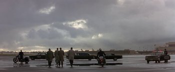 Movie still from “Nixon” (1995), directed by Oliver Stone – A group of people standing around a parking lot; Extreme Wide shot, Low angle