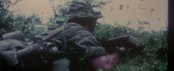 Movie still from “Nixon” (1995), directed by Oliver Stone – A man in a green jacket and hat is holding a rifle; Extreme Close Up shot, High angle