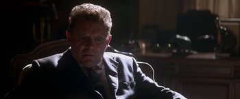 Movie still from “Nixon” (1995), directed by Oliver Stone – A man in a suit and tie sitting in a chair; Close Up shot, Low angle