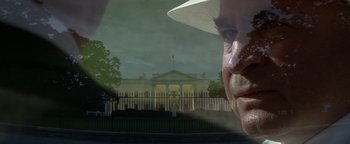 Movie still from “Nixon” (1995), directed by Oliver Stone – A man in a white hat looking out of a window at the white house; Extreme Close Up shot, Low angle