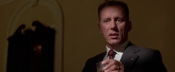 Movie still from “Nixon” (1995), directed by Oliver Stone – A person wearing a suit holding a glass; Close Up shot, Low angle