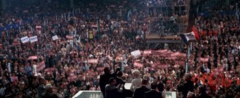 Movie still from “Nixon” (1995), directed by Oliver Stone – A crowd of people in a stadium with signs; Extreme Wide shot, High angle