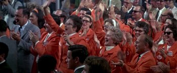 Movie still from “Nixon” (1995), directed by Oliver Stone – A group of people in red jackets are clapping and smiling; Medium shot, High angle