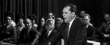 Movie still from “Nixon” (1995), directed by Oliver Stone – An old photo of a man speaking at a political event; Close Up shot, Over the shoulder angle