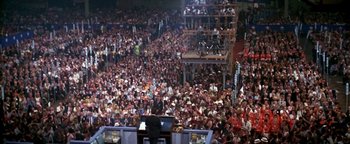 Movie still from “Nixon” (1995), directed by Oliver Stone – A large crowd of people in a large stadium; Extreme Wide shot, High angle