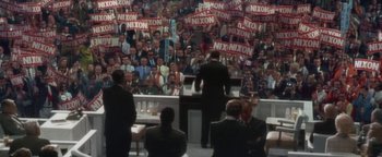 Movie still from “Nixon” (1995), directed by Oliver Stone – A crowd of people in front of a podium with nixon signs on them; Extreme Wide shot, High angle