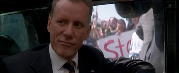 Movie still from “Nixon” (1995), directed by Oliver Stone – A person in a car with a crowd of people in the back of the car; Close Up shot, Low angle
