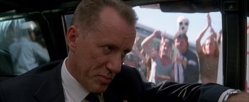 Movie still from “Nixon” (1995), directed by Oliver Stone – A person in a car with people in the background; Close Up shot, Low angle