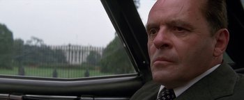 Movie still from “Nixon” (1995), directed by Oliver Stone – A man in a suit sitting in a car looking out the window; Close Up shot, Low angle