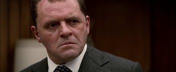 Movie still from “Nixon” (1995), directed by Oliver Stone – A man in a suit and tie looking at the camera; Close Up shot, Low angle