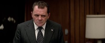 Movie still from “Nixon” (1995), directed by Oliver Stone – A person wearing a suit and tie; Close Up shot, Low angle