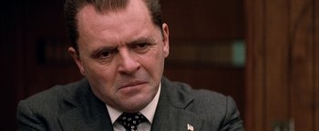 Movie still from “Nixon” (1995), directed by Oliver Stone – A man in a suit and tie sitting in a room; Close Up shot, Over the shoulder angle