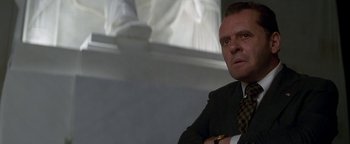 Movie still from “Nixon” (1995), directed by Oliver Stone – A man in a suit and tie sitting in front of a window; Close Up shot, Low angle
