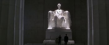 Movie still from “Nixon” (1995), directed by Oliver Stone – Two men are standing in front of a statue of abraham lincoln; Extreme Wide shot, Low angle
