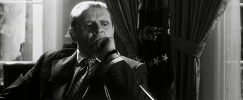 Movie still from “Nixon” (1995), directed by Oliver Stone – A man in a suit and tie holding his hand to his face; Close Up shot, Low angle