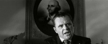 Movie still from “Nixon” (1995), directed by Oliver Stone – A man in a suit and tie in front of a portrait of a man; Close Up shot, Low angle