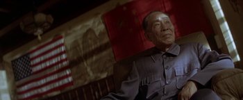 Movie still from “Nixon” (1995), directed by Oliver Stone – An older man sitting in a chair in front of a flag; Medium shot, Low angle