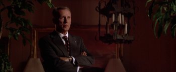 Movie still from “Nixon” (1995), directed by Oliver Stone – A man in a suit and tie with his arms crossed; Medium shot, Low angle