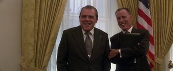 Movie still from “Nixon” (1995), directed by Oliver Stone – A man in a suit standing next to another man in a suit; Medium shot, Low angle