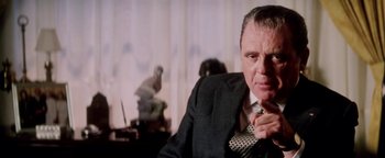 Movie still from “Nixon” (1995), directed by Oliver Stone – An older man wearing a suit and tie in a room; Close Up shot, Low angle