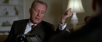 Movie still from “Nixon” (1995), directed by Oliver Stone – A man in a suit and tie holding his hand up; Close Up shot, Low angle