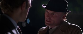 Movie still from “Nixon” (1995), directed by Oliver Stone – A man wearing a hat and a trench coat talking to another man; Close Up shot, Over the shoulder angle