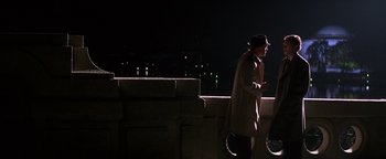 Movie still from “Nixon” (1995), directed by Oliver Stone – A man in a trench coat standing on the side of a building; Wide shot, Over the shoulder angle