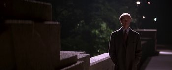 Movie still from “Nixon” (1995), directed by Oliver Stone – A man in a suit standing next to a railing at night; Medium shot, Over the shoulder angle