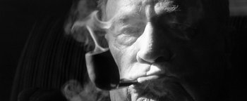 Movie still from “Nixon” (1995), directed by Oliver Stone – An old man smoking a pipe in a black and white photo; Extreme Close Up shot, Low angle