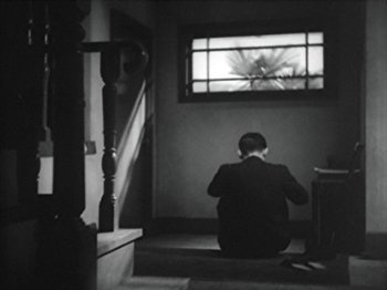 Movie still from “No Regrets for Our Youth” (1946), directed by Akira Kurosawa – A man sitting on the stairs looking out a window; Wide shot, Low angle