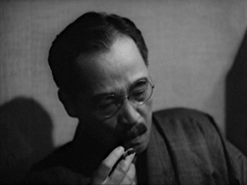 Movie still from “No Regrets for Our Youth” (1946), directed by Akira Kurosawa – An older man with glasses is holding his finger to his mouth; Close Up shot, Low angle