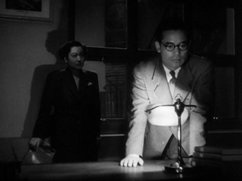Movie still from “No Regrets for Our Youth” (1946), directed by Akira Kurosawa – A man and a woman are standing at a desk; Medium shot, Low angle