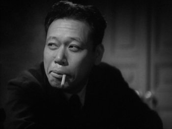 Movie still from “No Regrets for Our Youth” (1946), directed by Akira Kurosawa – An older man smoking a cigarette while sitting down; Close Up shot, Low angle