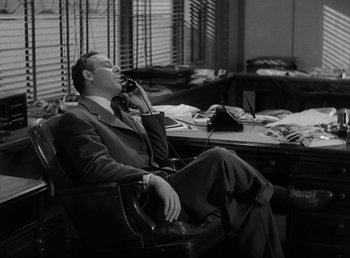 Movie still from “No Time for Love” (1943), directed by Mitchell Leisen – A black and white photo of a man sitting in an office chair talking on the phone; Medium shot, High angle