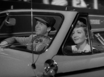 Movie still from “No Time for Love” (1943), directed by Mitchell Leisen – A man and a woman sitting in the drivers seat of a car; Medium shot, High angle