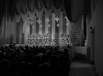 Movie still from “No Time for Love” (1943), directed by Mitchell Leisen – A black - and - white photo of a stage with people watching; Extreme Wide shot, Low angle