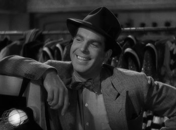 Movie still from “No Time for Love” (1943), directed by Mitchell Leisen – A man wearing a suit and a hat smiling for the camera; Close Up shot, Over the shoulder angle