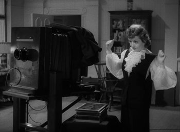 Movie still from “No Time for Love” (1943), directed by Mitchell Leisen – A black - and - white photo of a woman in front of a television; Medium shot, Low angle