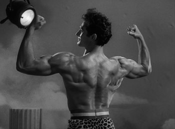 Movie still from “No Time for Love” (1943), directed by Mitchell Leisen – A black and white photo of a man flexing his muscles; Medium shot, Low angle